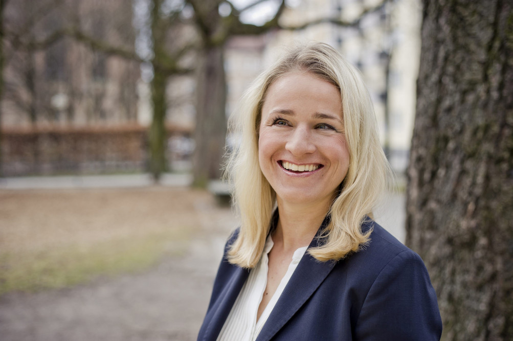 Eine Frau mit blonden, langen Haaren, einem blauen Sakko und einer weißen Bluse lächelt.