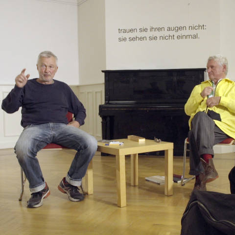 „Thomas Braun hat weiße Haare und einen kurzen Bart, er redet und
gestikuliert. Gert Conradt hat weiße kurze Haare und trägt eine gelbe Jacke, er schaut
aufmerksam Thomas Braun zu.